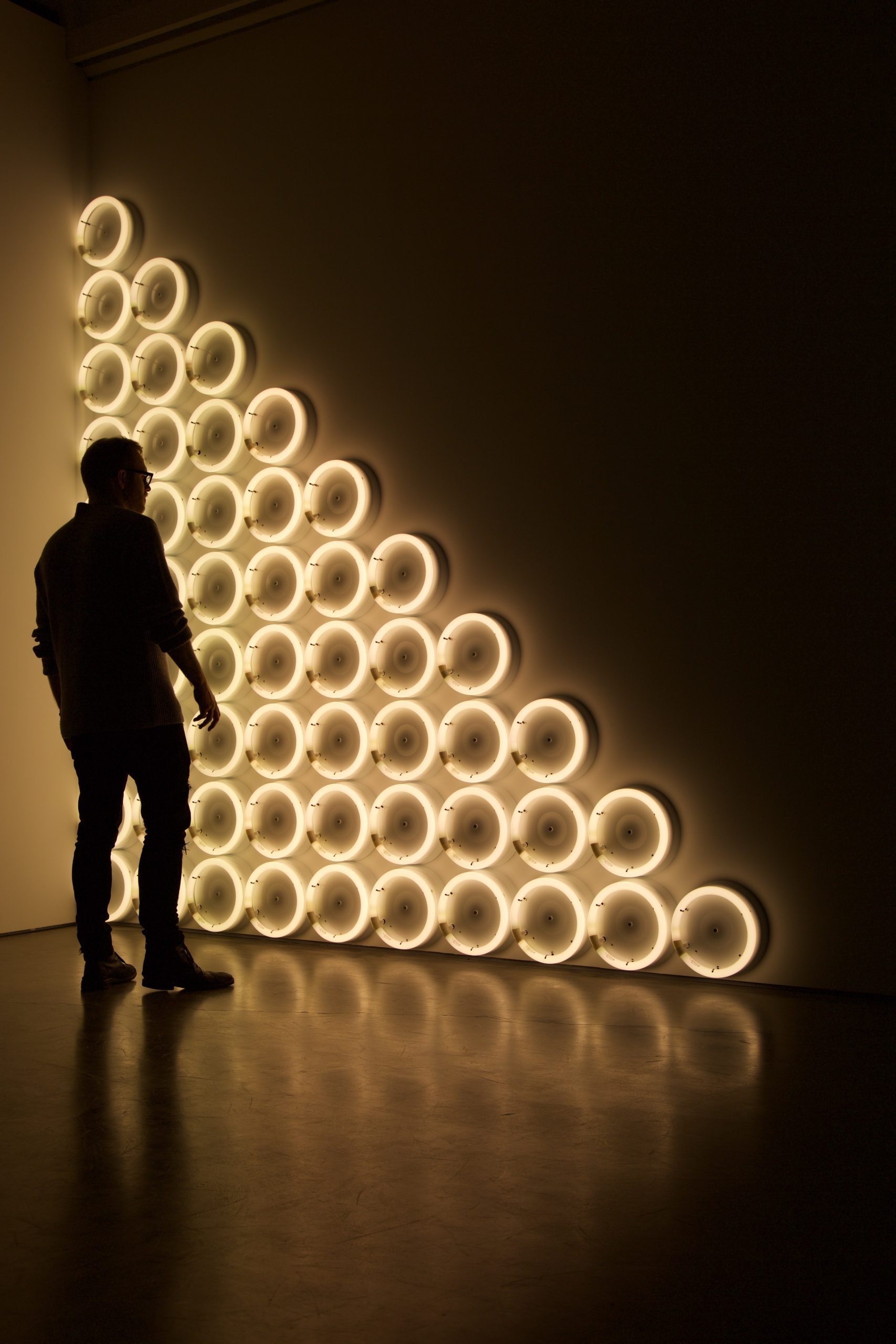 A man standing in front of a wall with stacked circular white lights