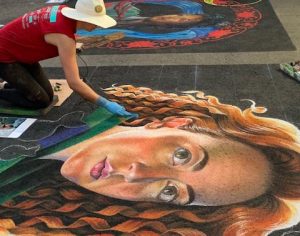 A person using chalk to create a mural of a red haired woman