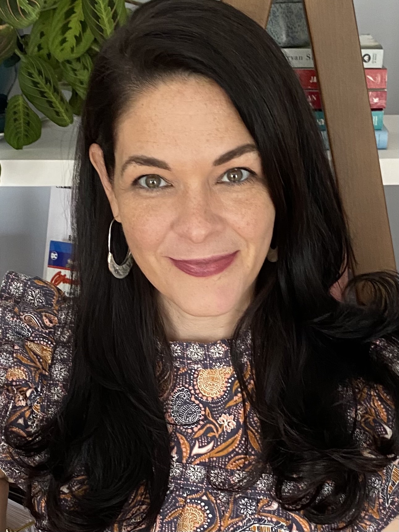 Smiling dark haired woman with earrings and a paisley printed top