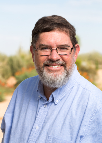 A man with short brown hair and a gray beard with glasses and a light blue button up top