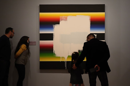 People standing in front of a large canvas painted red, green, blue, yellow and purple with a white box painted over the center